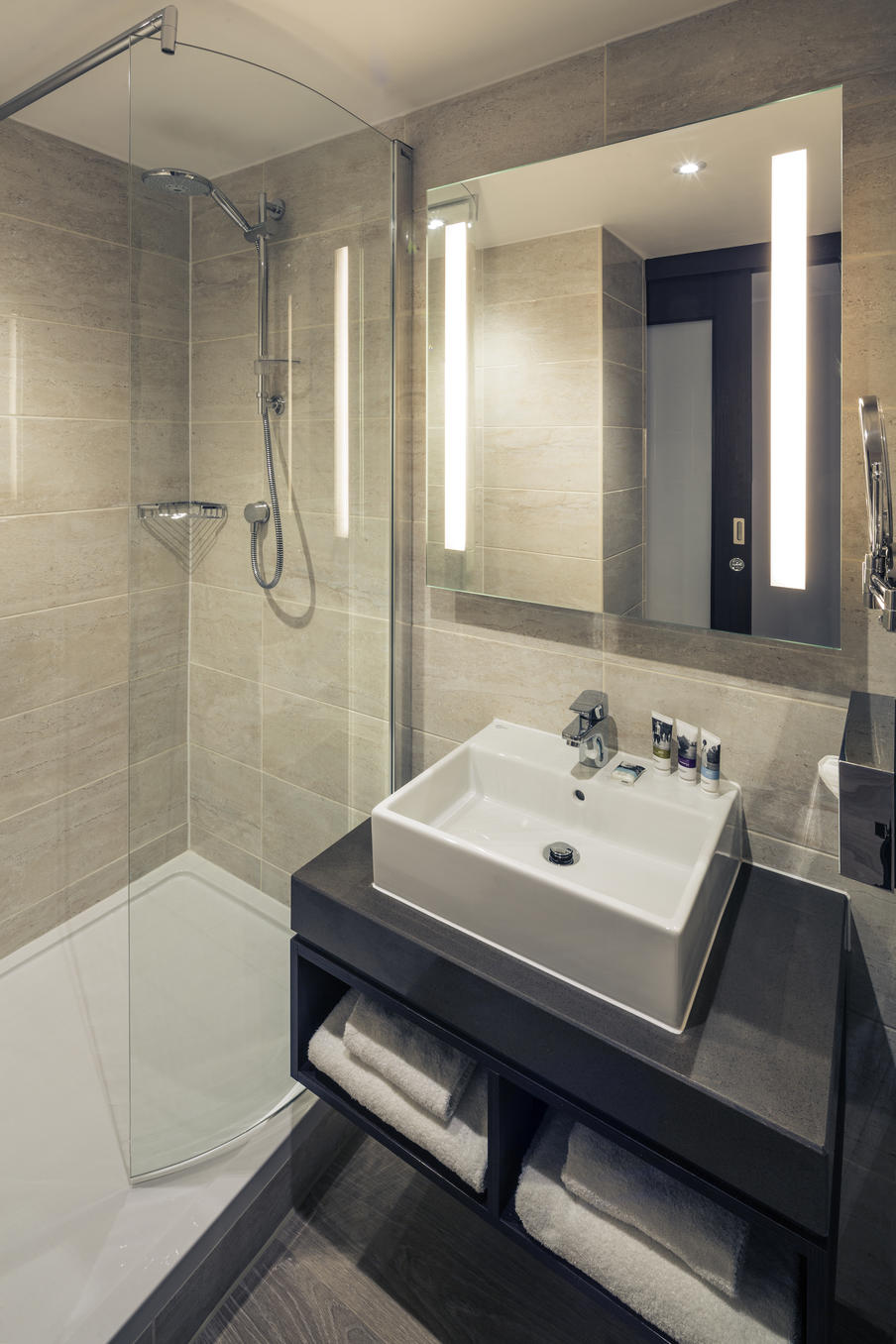 Modern shower room themed in gray with rectangle sink with travel size shampoo and conditioner, white towels.