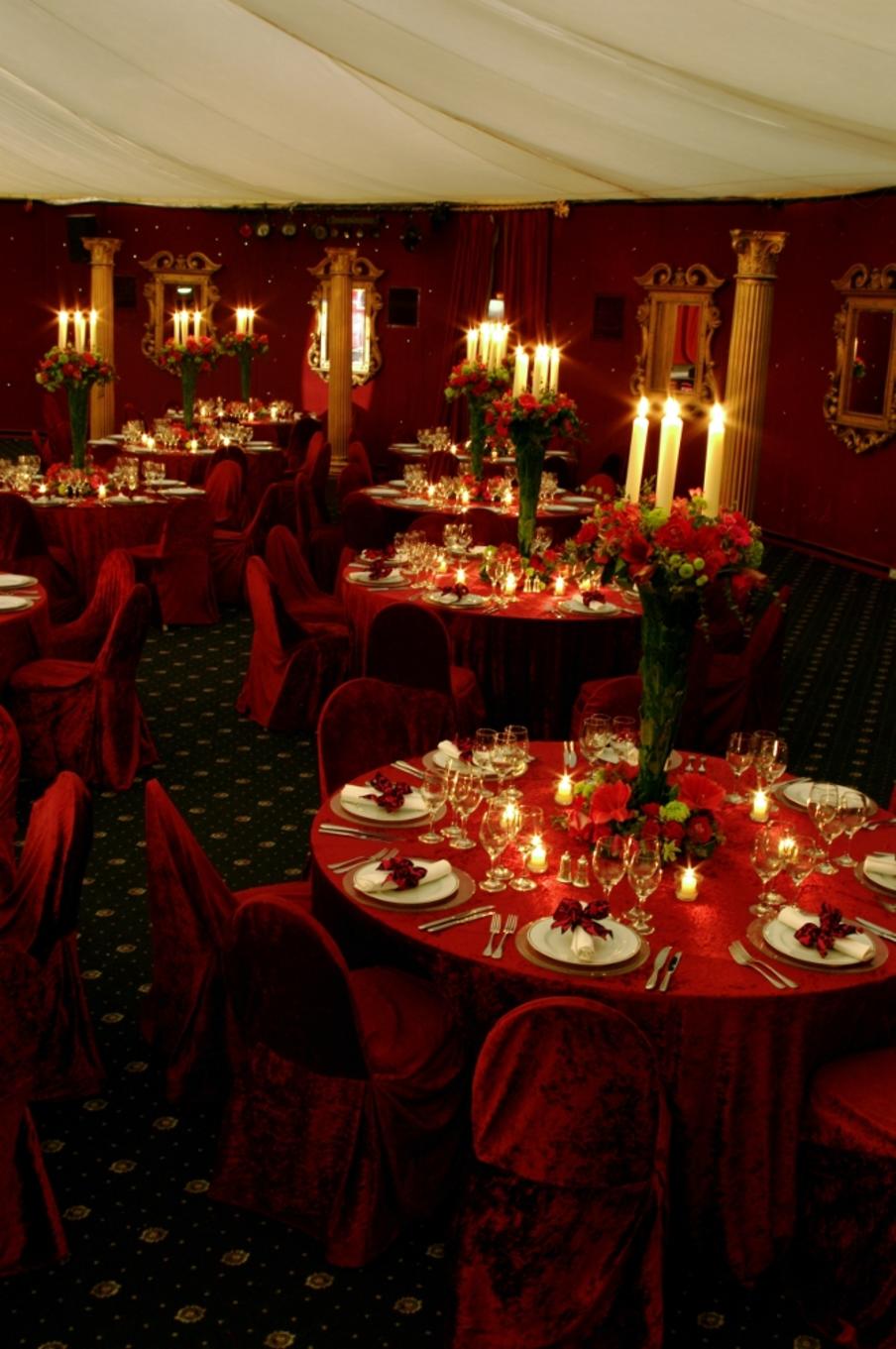 A red theme for dinner set on round tables with large centerpiece floral and candle decoration on each table