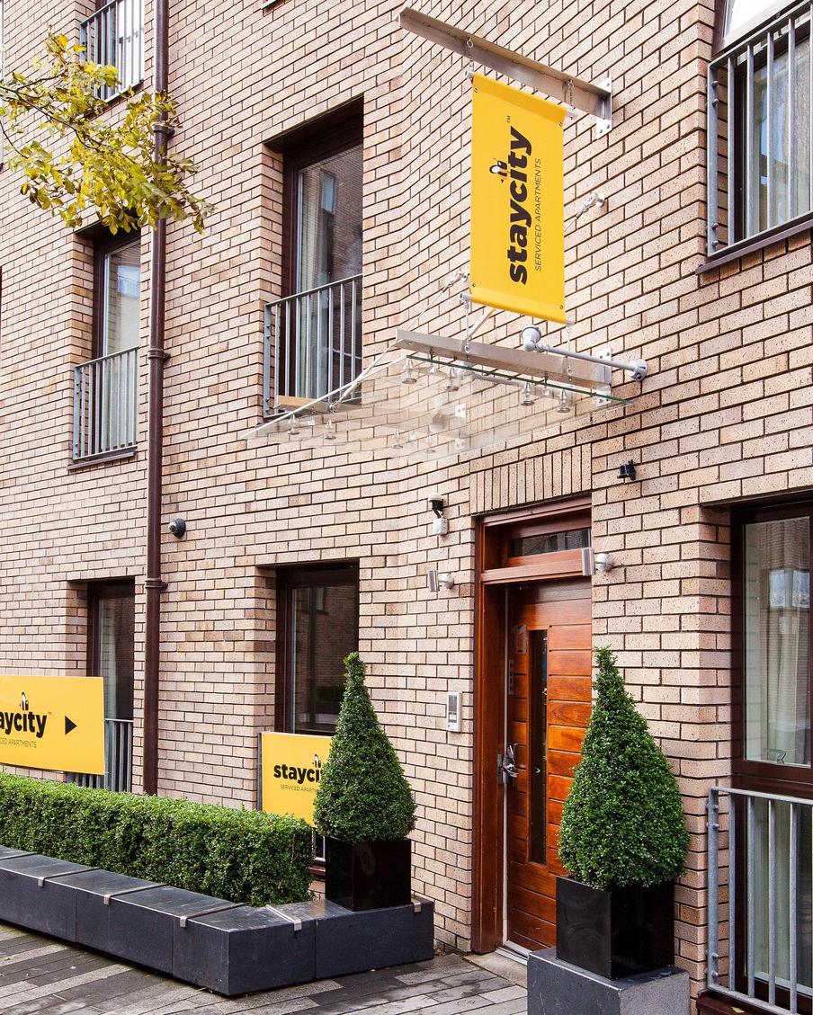 Entrance to apartments within a modern building with feature plants either side of the door and outside seating area.