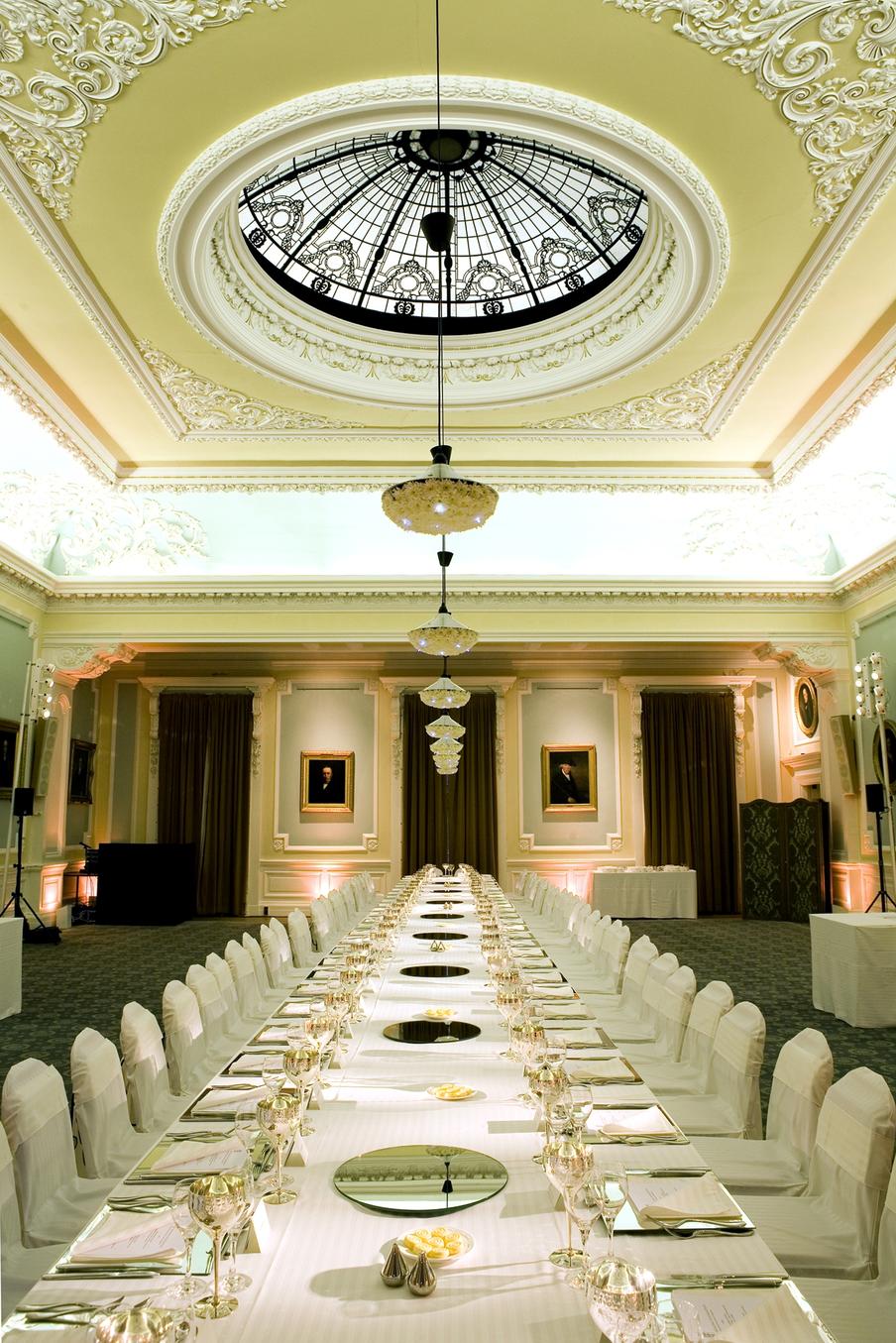 Long banqueting table set for dinner within a Georgian Period room with portraits set in gold gilt frames set around the walls.