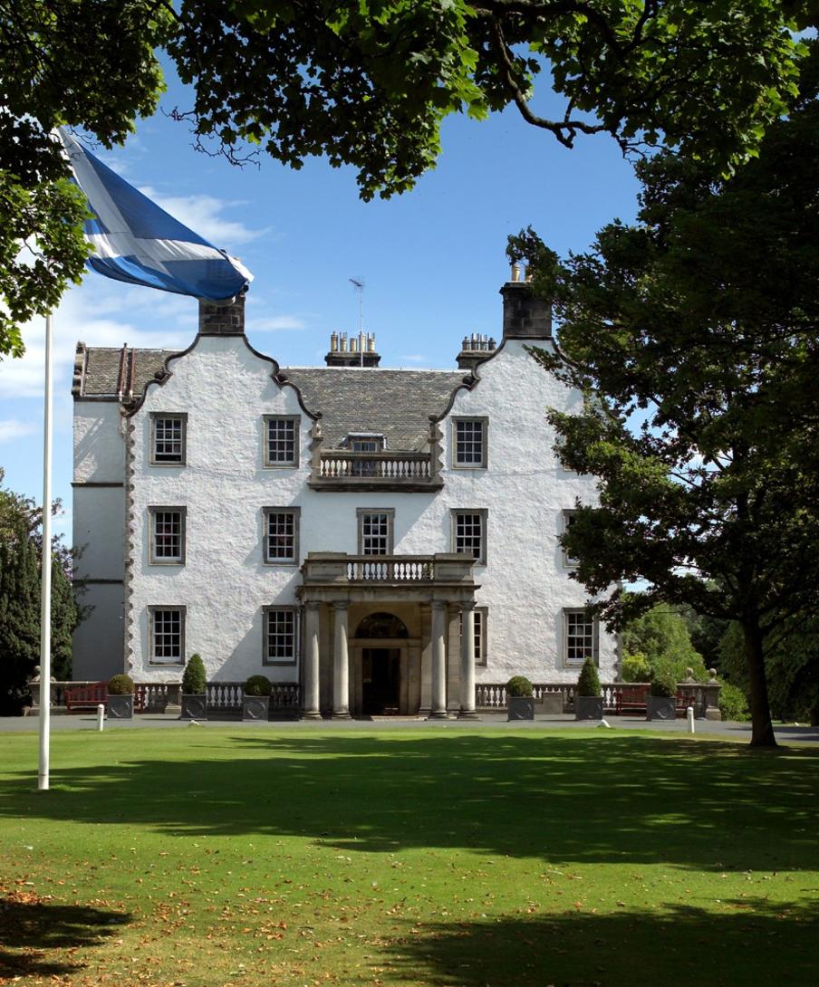 A view to the hotel entrance over green parkland in the sunshine with established trees and shrubs