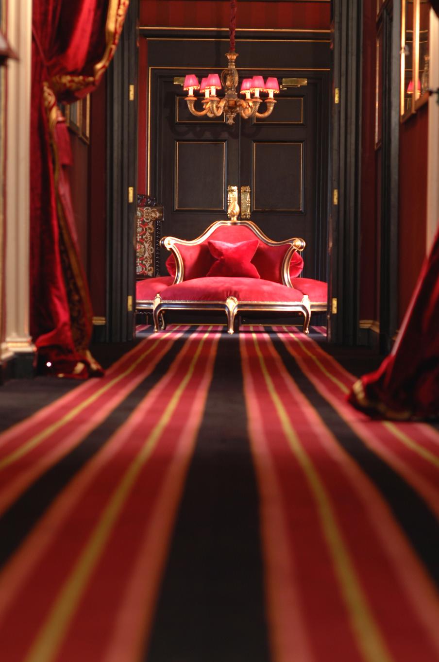 Looking down the hotel corridor to a feature seating area within the reception of the hotel with striped carped with red, black and gold theming