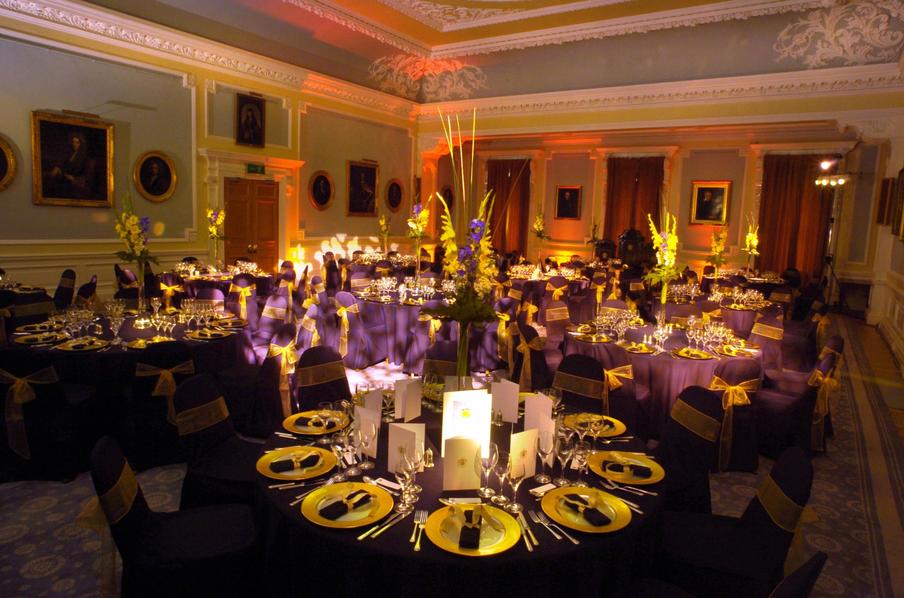 Playfar Hall set for dinner with black table linen and  themed lighting.  Each plate set with napkin and menu card.