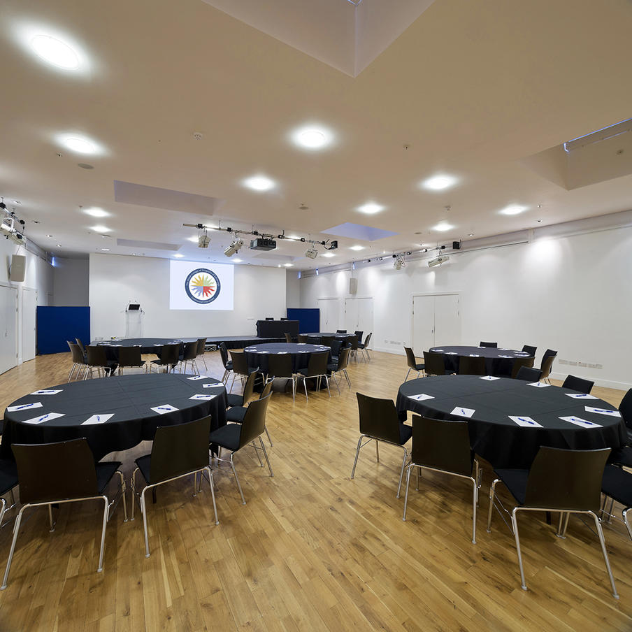 Wolfson Hall set up cabaret style with screen, overhead projector and black cloths and chairs.