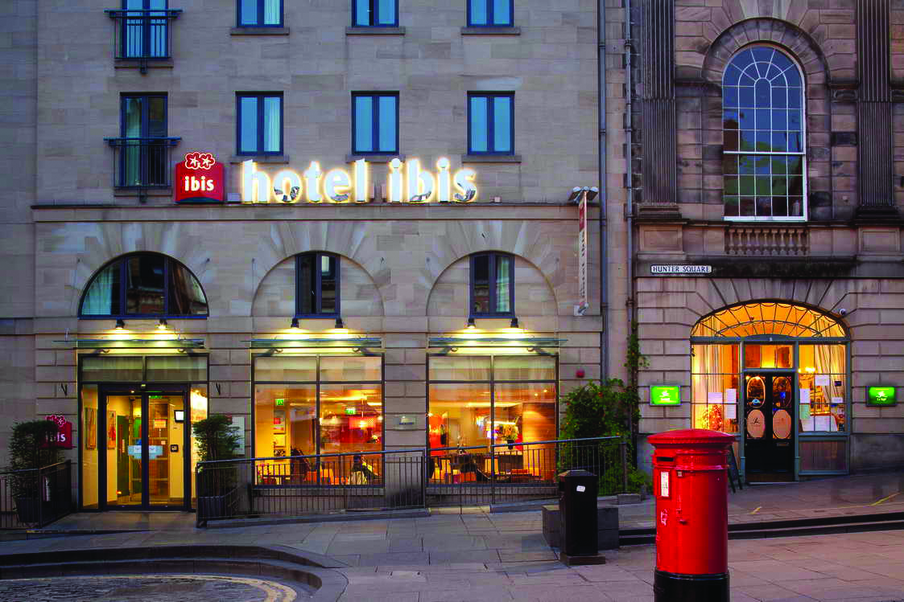 Early evening view of hotel with red pillar box in the foreground and set back off a part cobbled street. A view into the hotel through large windows.
