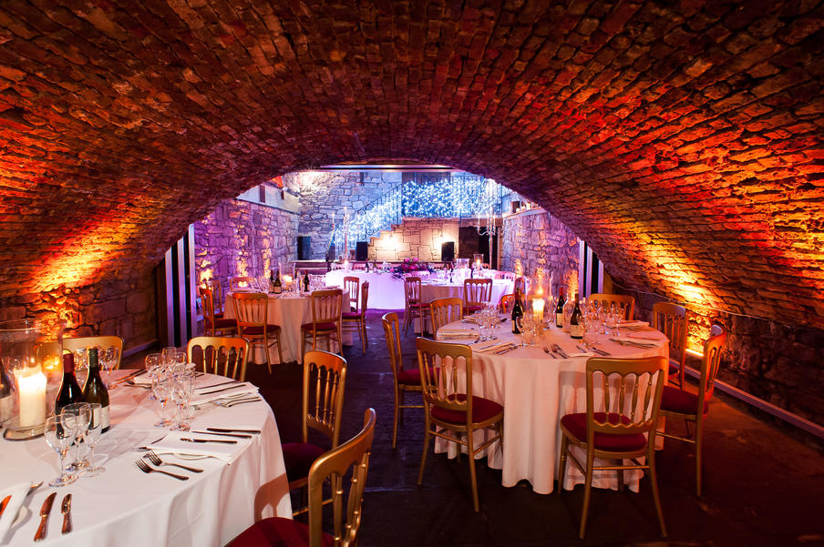 vaulted ceiling dinner setting with feature brick work, round tables with gold and red chairs and candle lit theme.