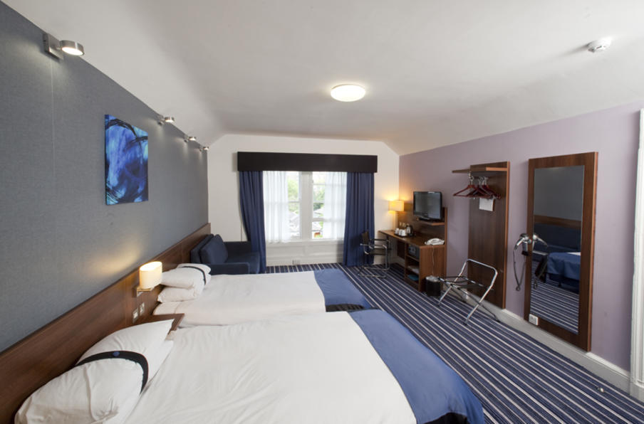 Large room with twin double beds, blue colour theme with large windows, desk and luggage rack.