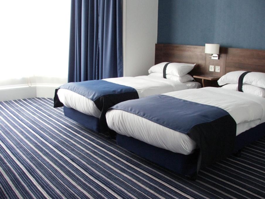 Twin single bed room with blue theme and large windows.  Bedside tables and lamps between the beds.