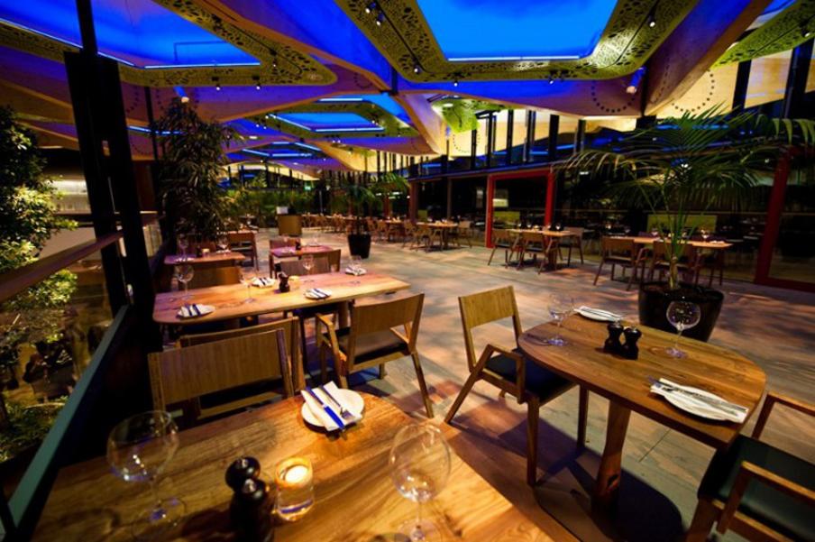 Restaurant with outlook over gardens with feature wooden furniture and decorative ceiling. Set on an elevated balcony looking onto a botanical theme exhibition.