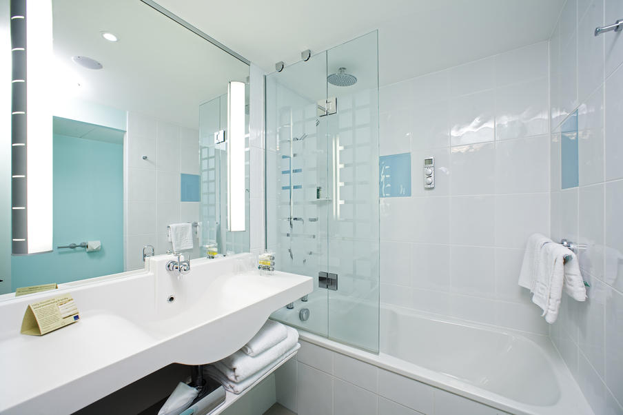 Modern bathroom with shower over bath, white and aqua tiling and fresh white towels.
