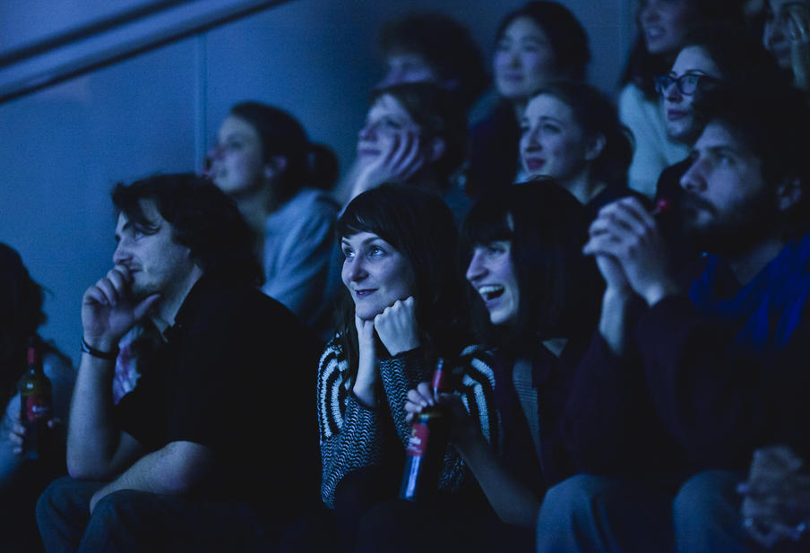 Edinburgh University: Woman smiling thoughtfully in audience at event. The room is lit in deep blue.