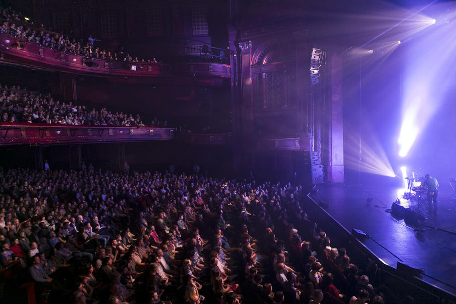 Edinburgh Playhouse: A large traditional theatre with three tiers in a purple glow with a full audience watching a performance on stage.