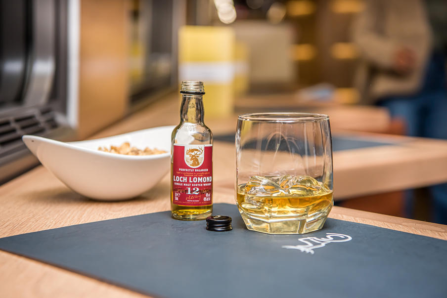 A glass and small bottle of whisky next to a snack bowl in the dining car