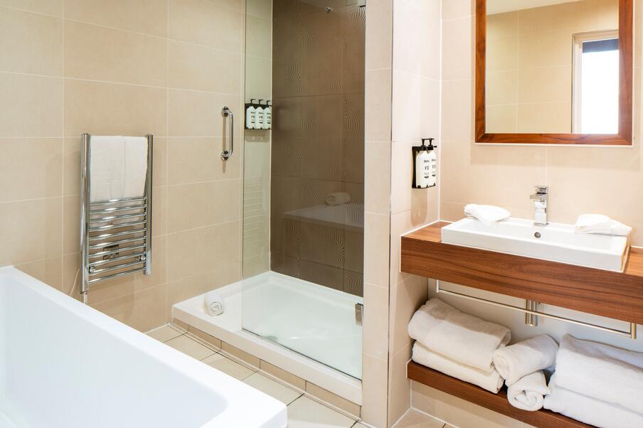 Image of hotel room bathroom, with a white bath tub, walk in shower and white sink on wooden counter top.