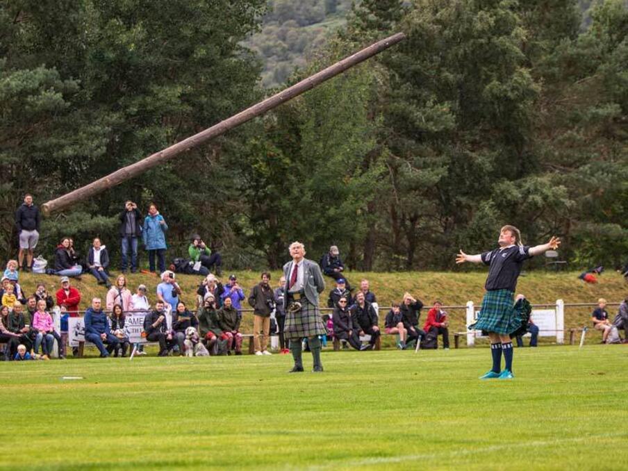 Man throws a log across the field in front of a crowd during Highland games.